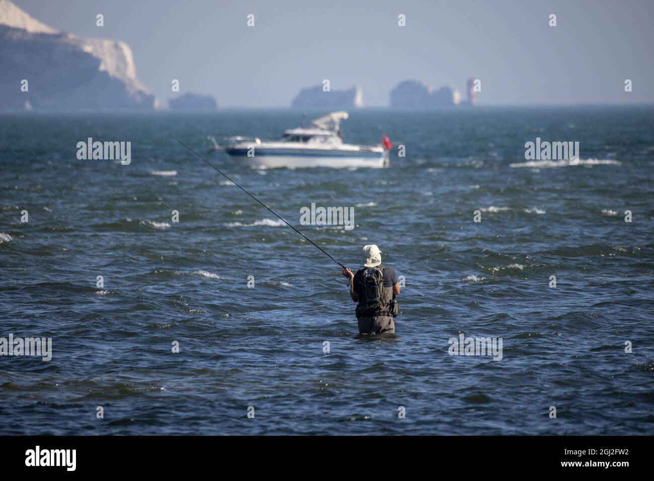 A fisherman in waders casts his line out in the Solent shallow stretch of tidal water with Isle of Weight in distance, Hampshire and Dorset coastline. Stock Photo