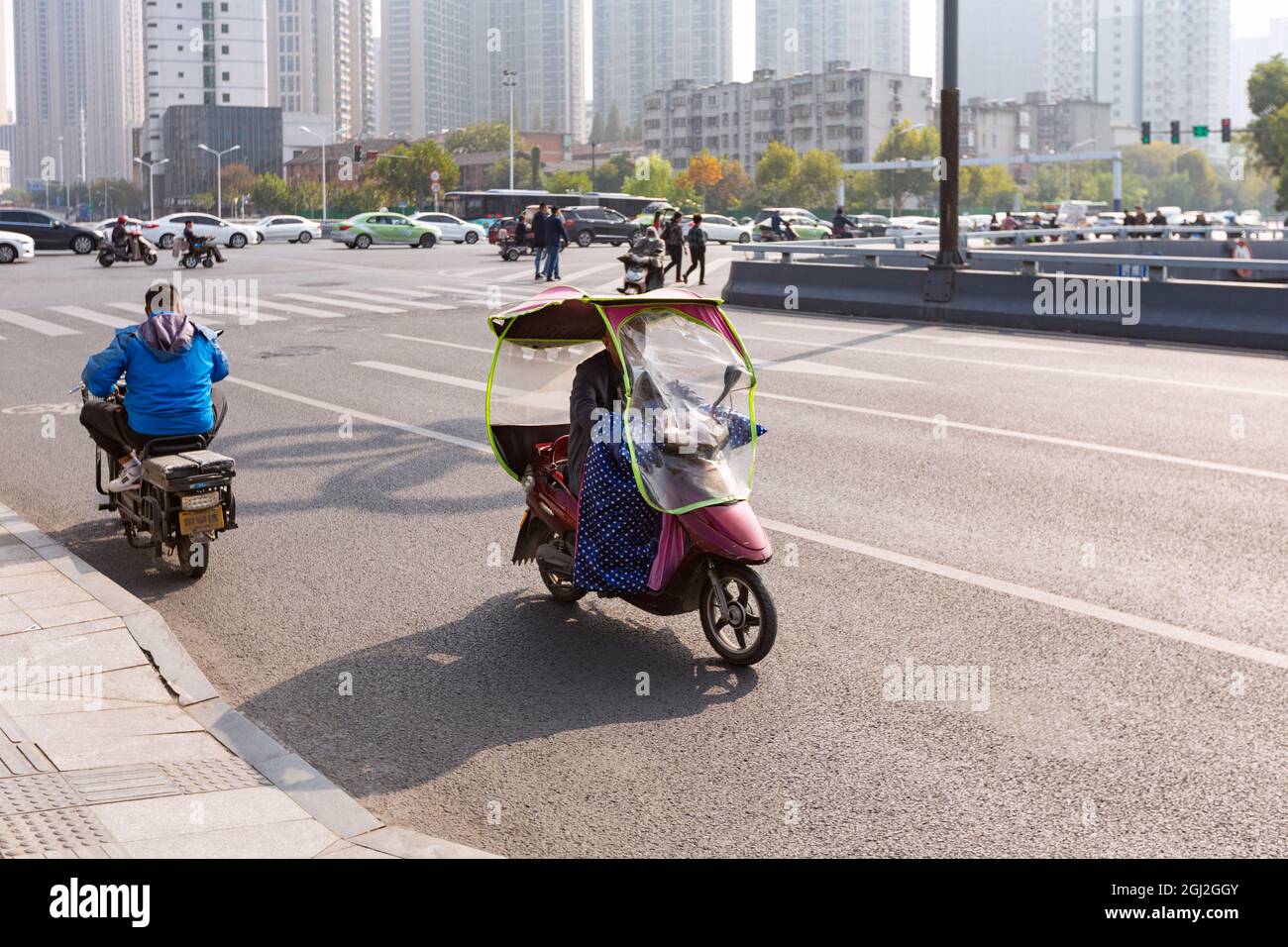 People on electric bicycle with colourful windshield on crossroad, Hefei, China. Stock Photo
