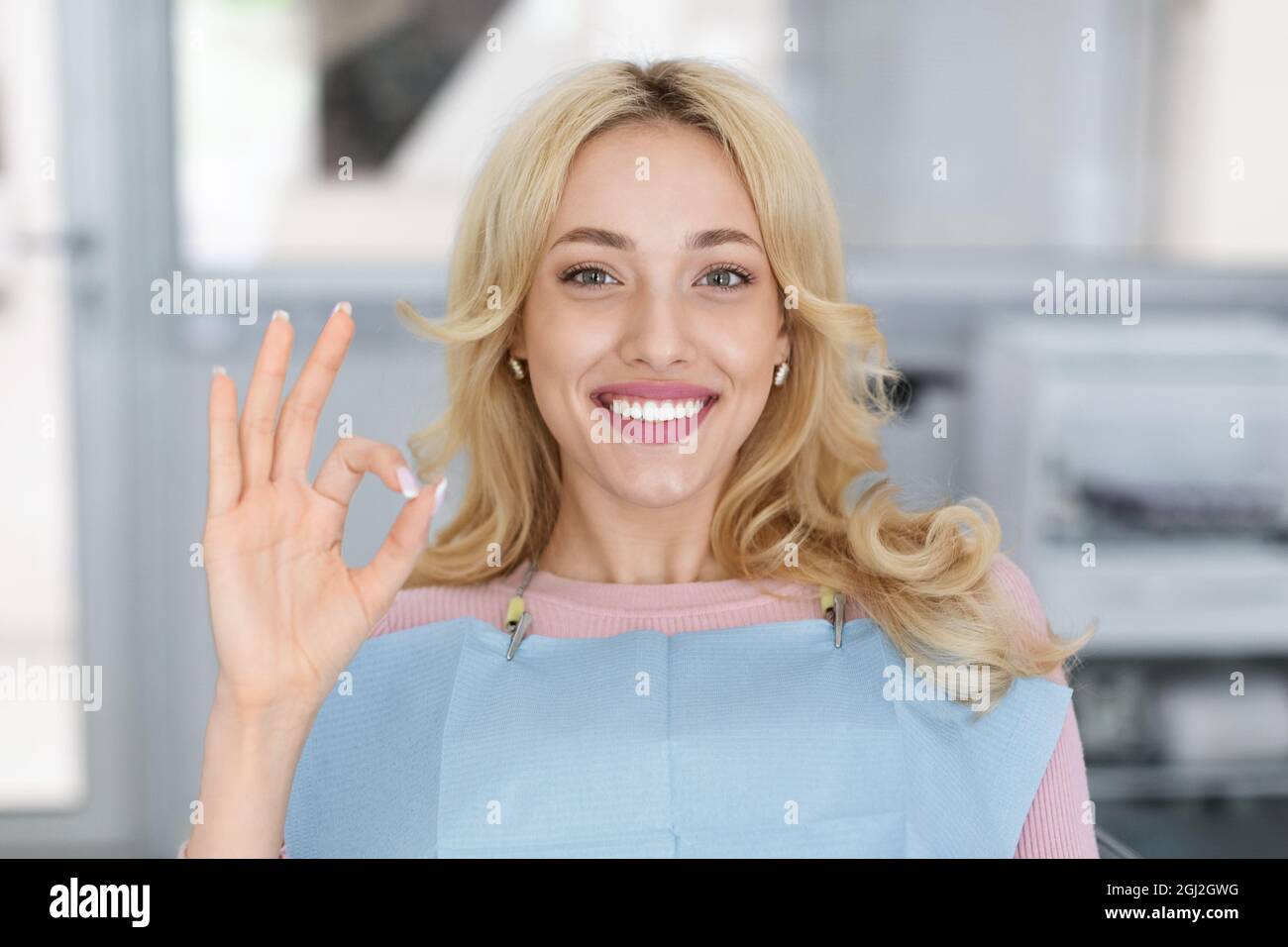 Closeup portrait of happy attractive millennial woman visiting modern dental clinic, showing her beautiful white smile and camera and showing okay ges Stock Photo