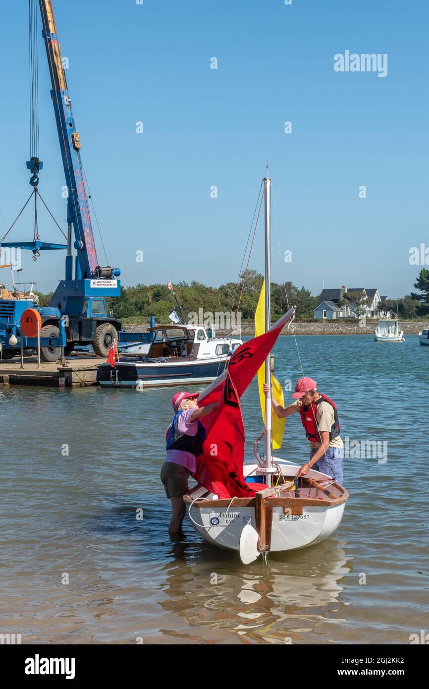 Couple taking down the sails of a sailing dinghy as they arrive in Keyhaven, Hampshire, England, UK Stock Photo