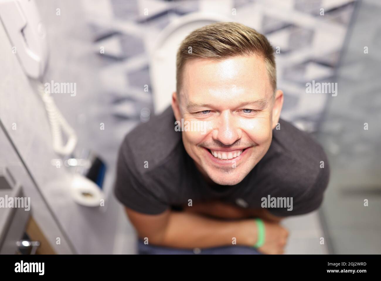 Portrait of young contented man sitting on toilet closeup Stock Photo