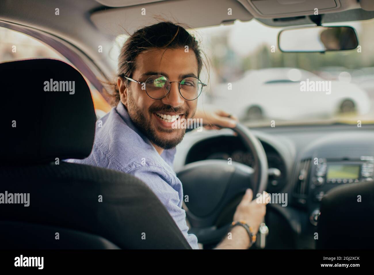 Cheerful middle-eastern young man taxi driver looking at back seat and  smiling at camera, closeup photo, copy space. Happy arab guy enjoying his  brand Stock Photo - Alamy