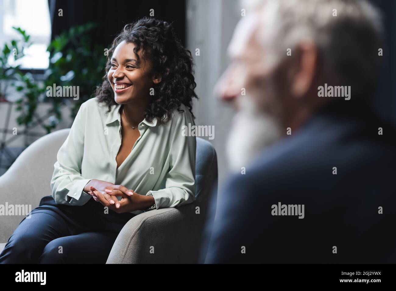 cheerful african american journalist sitting in armchair near blurred