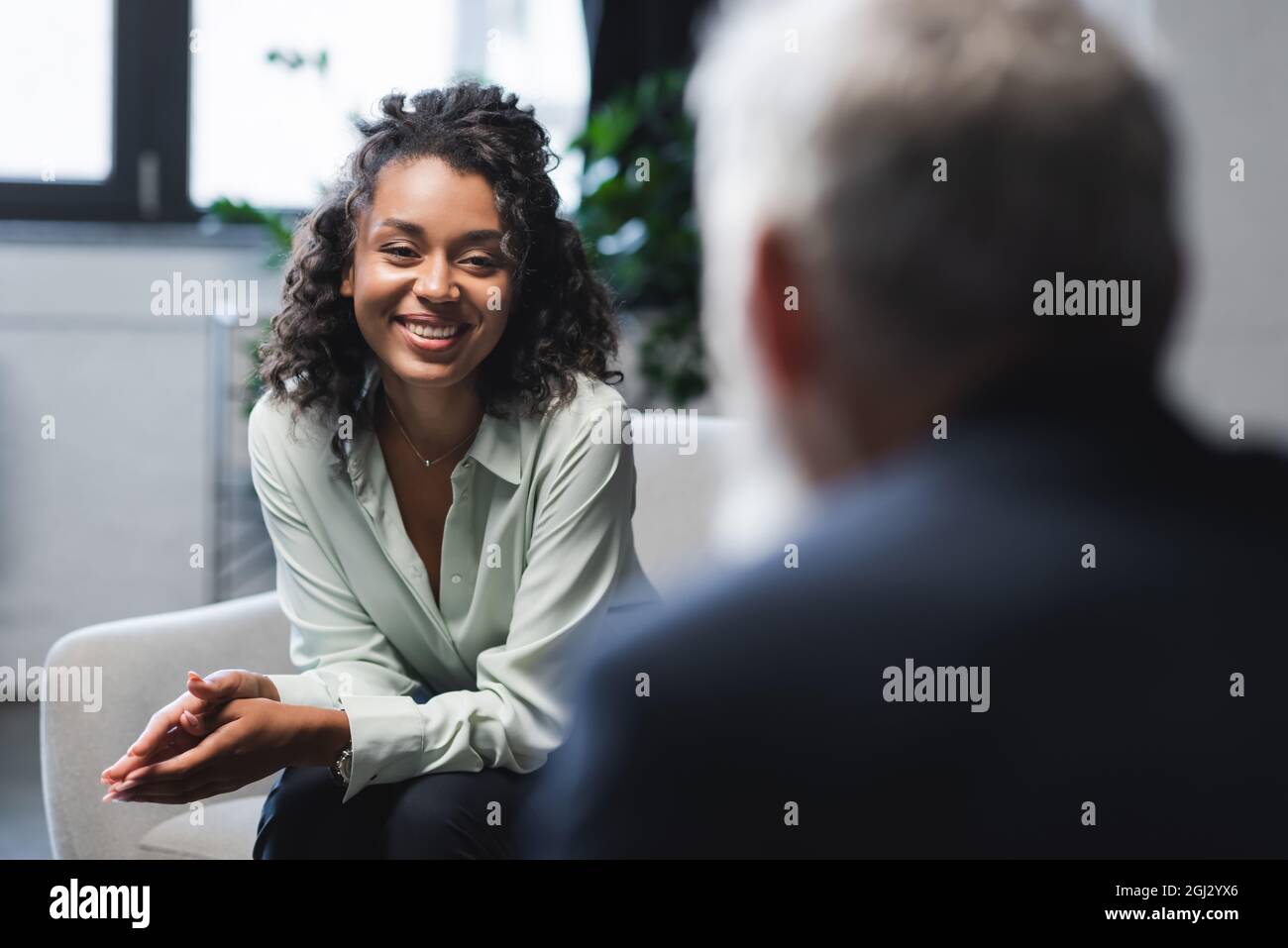 joyful african american journalist sitting in armchair and smiling near