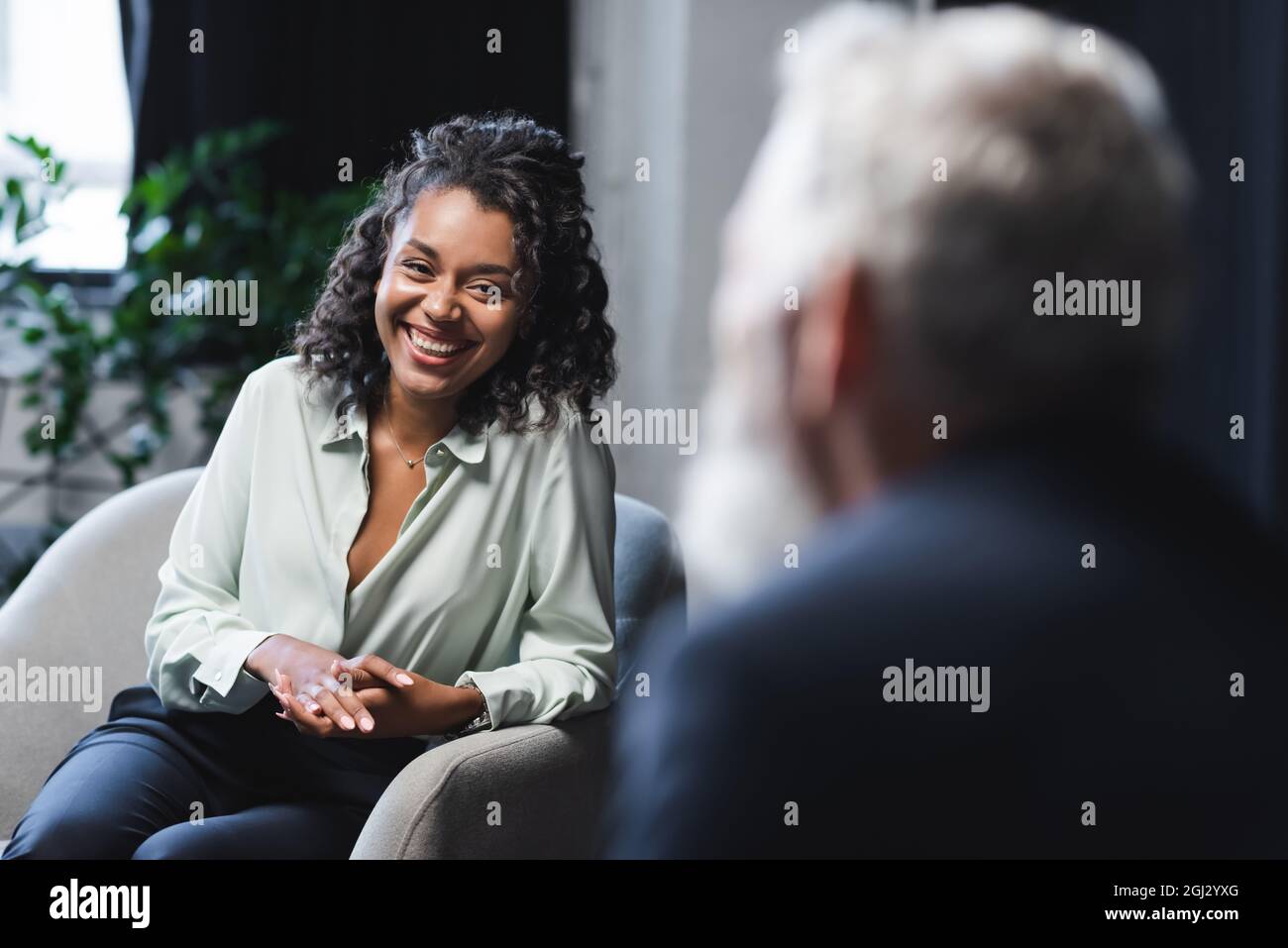 positive african american journalist sitting in armchair and smiling