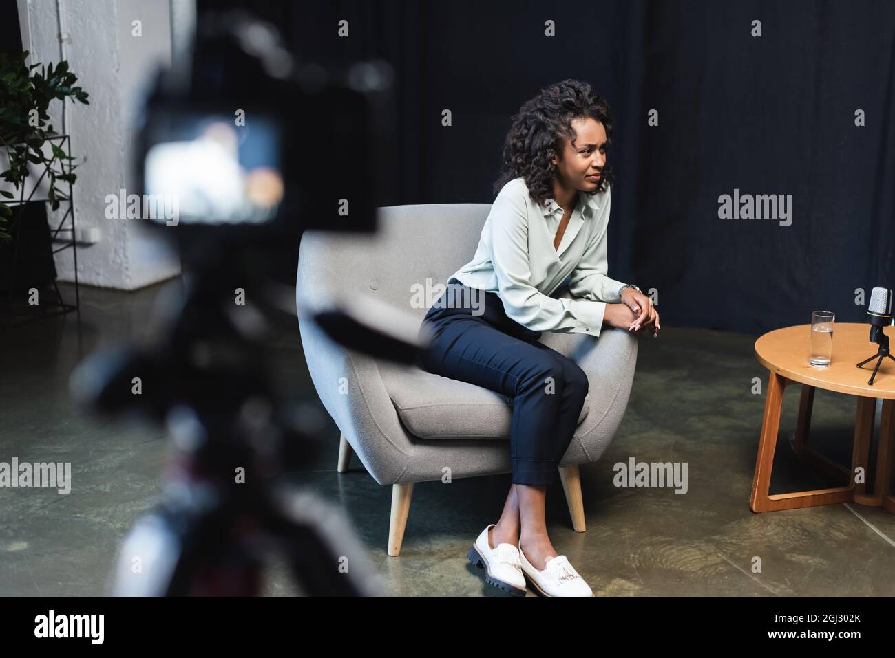 curly african american journalist sitting in armchair near coffee table