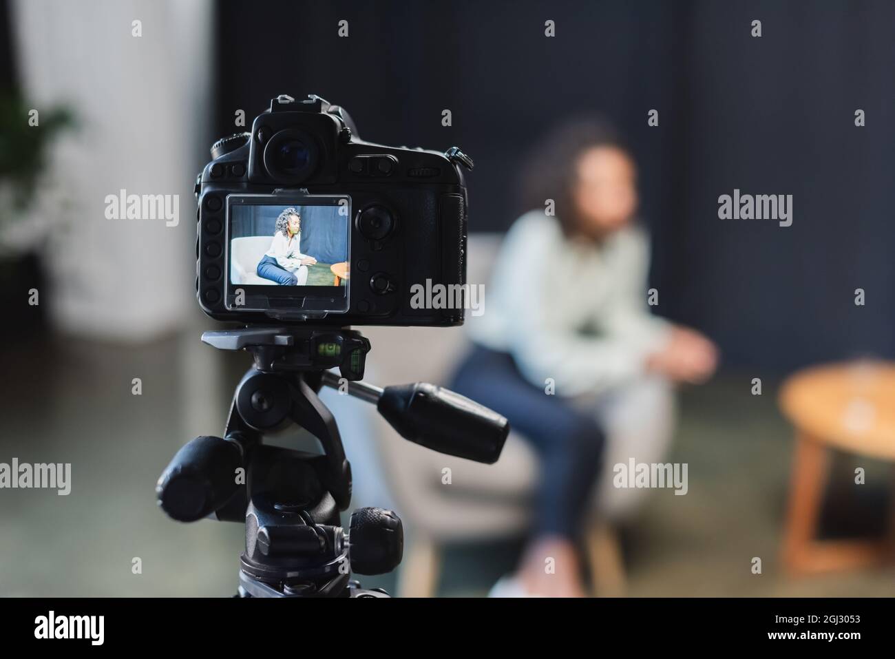 curly african american journalist sitting in armchair near blurred