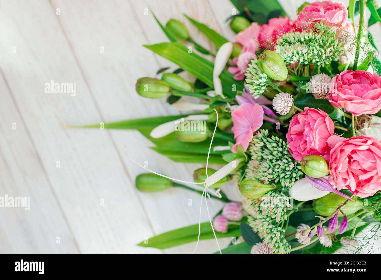 Bouquet of pink white green flowers arranged on wooden background. Roses, sedum, hosta, seed pods, gomphrena and grasses Stock Photo