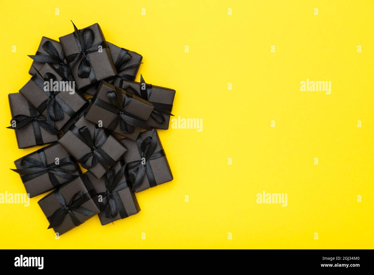 Black gift boxes with black ribbons on bright rich yellow background. Black Friday sale flat lay, top view, copy space Stock Photo