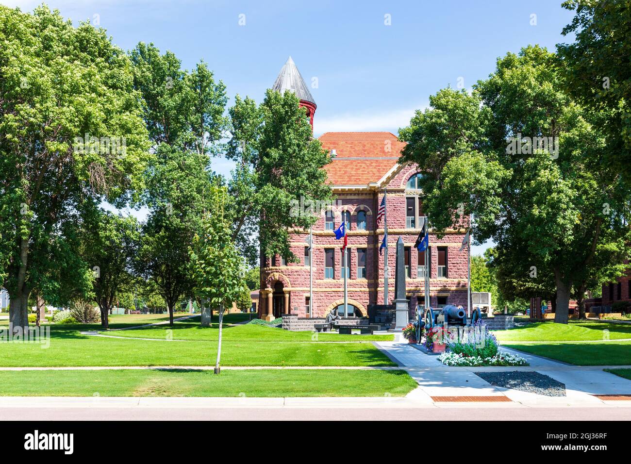 LUVERNE, MN, USA-21 AUGUST 2021: Rock County Courthouse, built of local quartzite, with memorials and cannon.  Blue sky and lush greenery.. Stock Photo