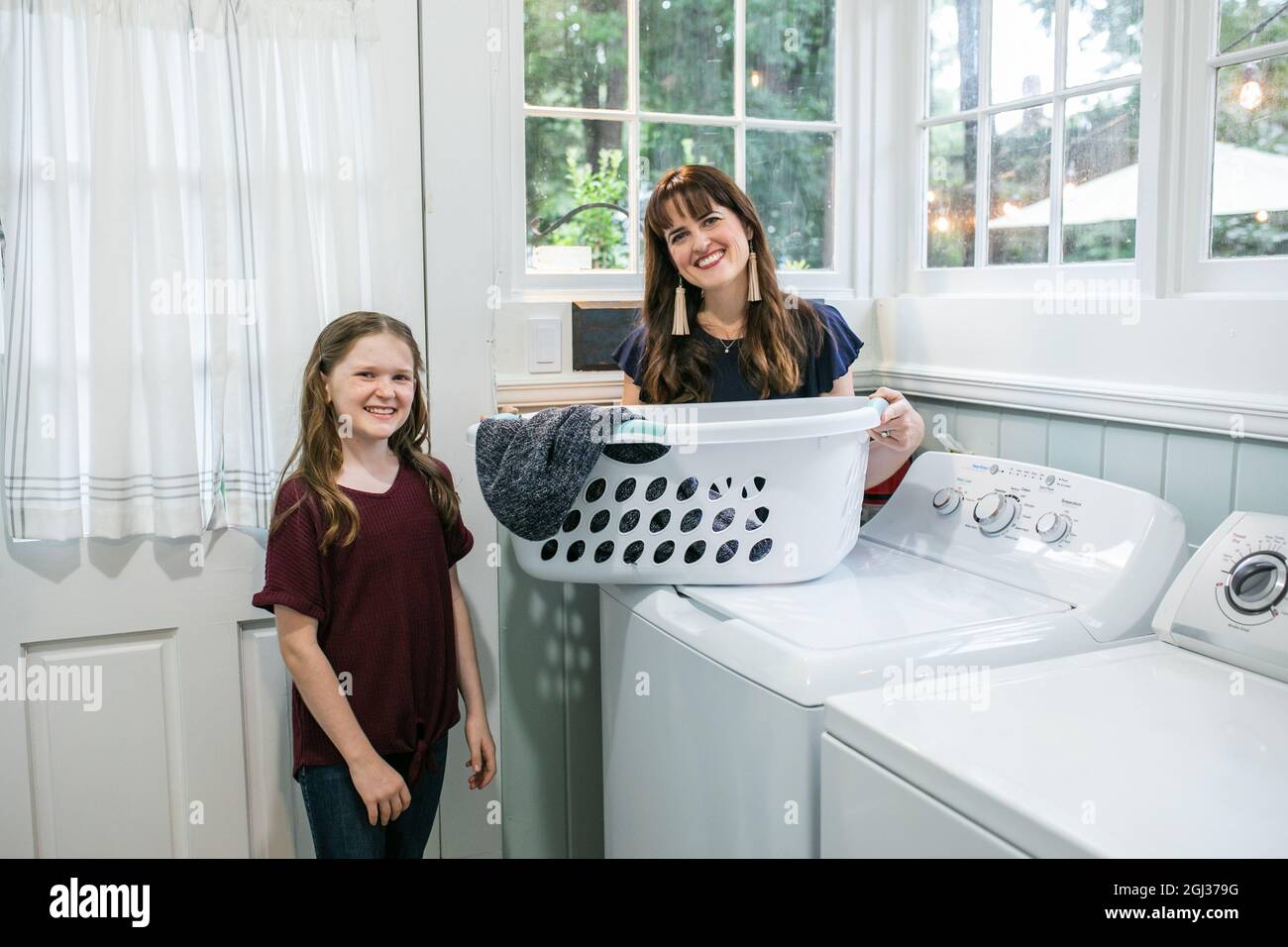 A mother and daughter doing laundry chores together in their natural light laundry room Stock Photo