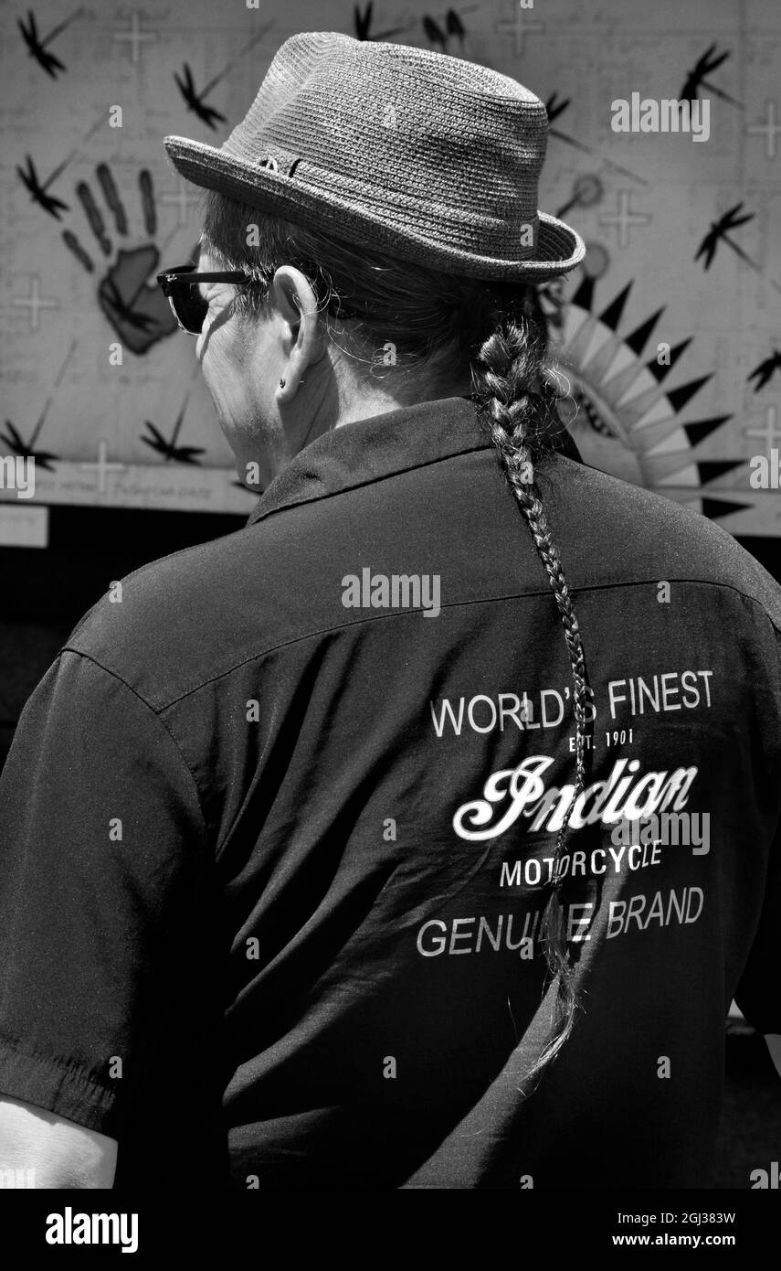A Native American artist with braided hair wears an Indian Motorcycle shirt and stands in his booth at an outdoor art sale in Santa Fe, New Mexico. Stock Photo