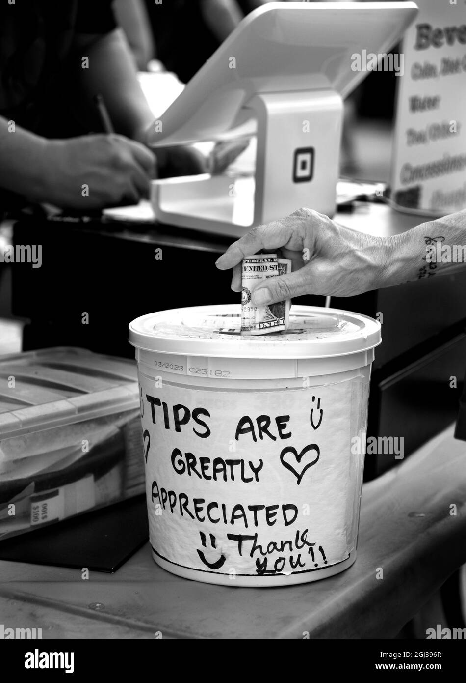 A customer places a dollar bill into a tip jar or tip bucket at an outdoor food vendor's booth in Santa Fe, New Mexico. Stock Photo