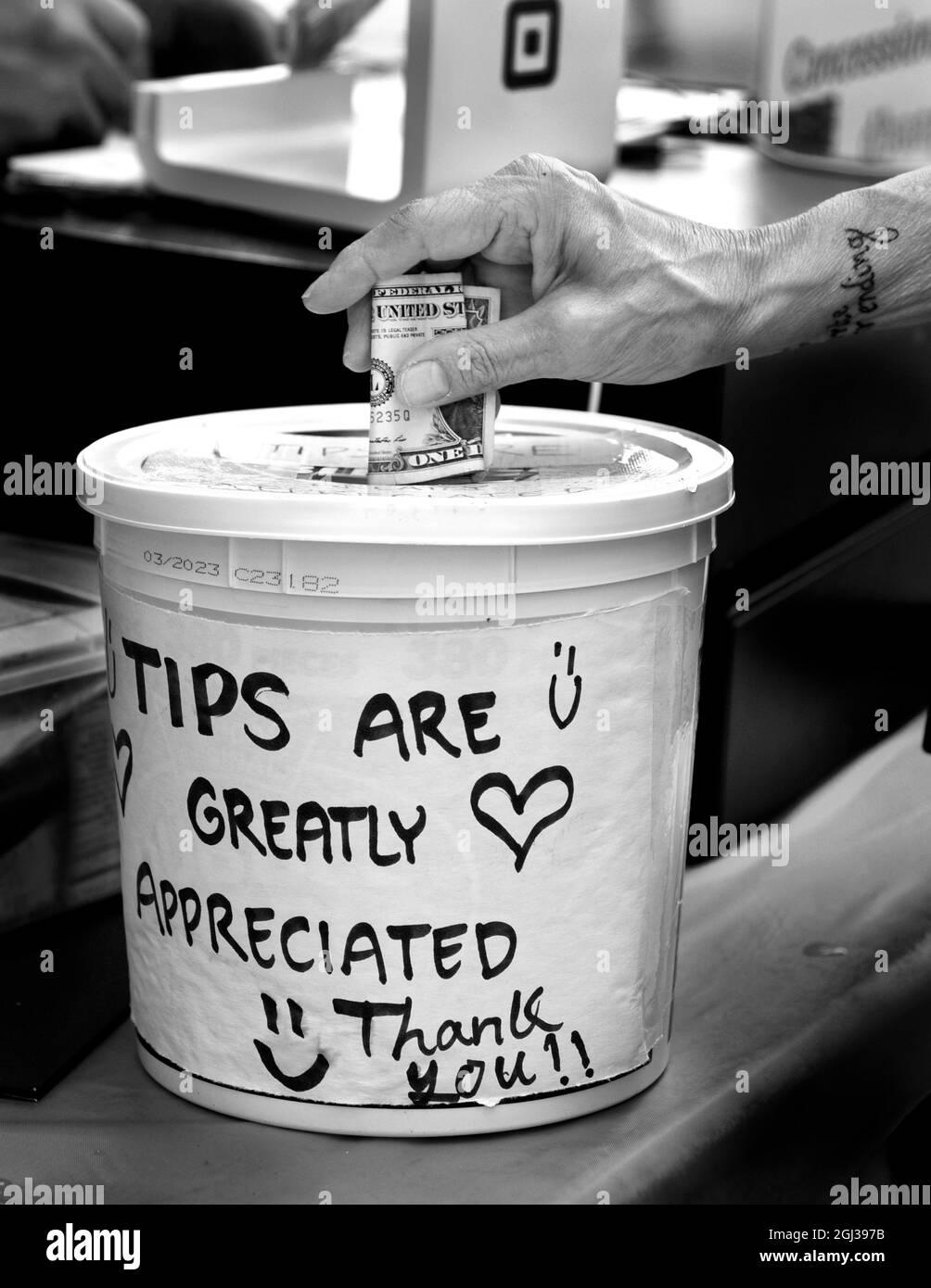 A customer places a dollar bill into a tip jar or tip bucket at an outdoor food vendor's booth in Santa Fe, New Mexico. Stock Photo