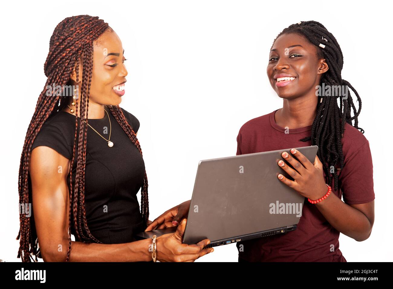 two smiling beautiful sisters standing in burgundy black and red colors holding and using a laptop Stock Photo