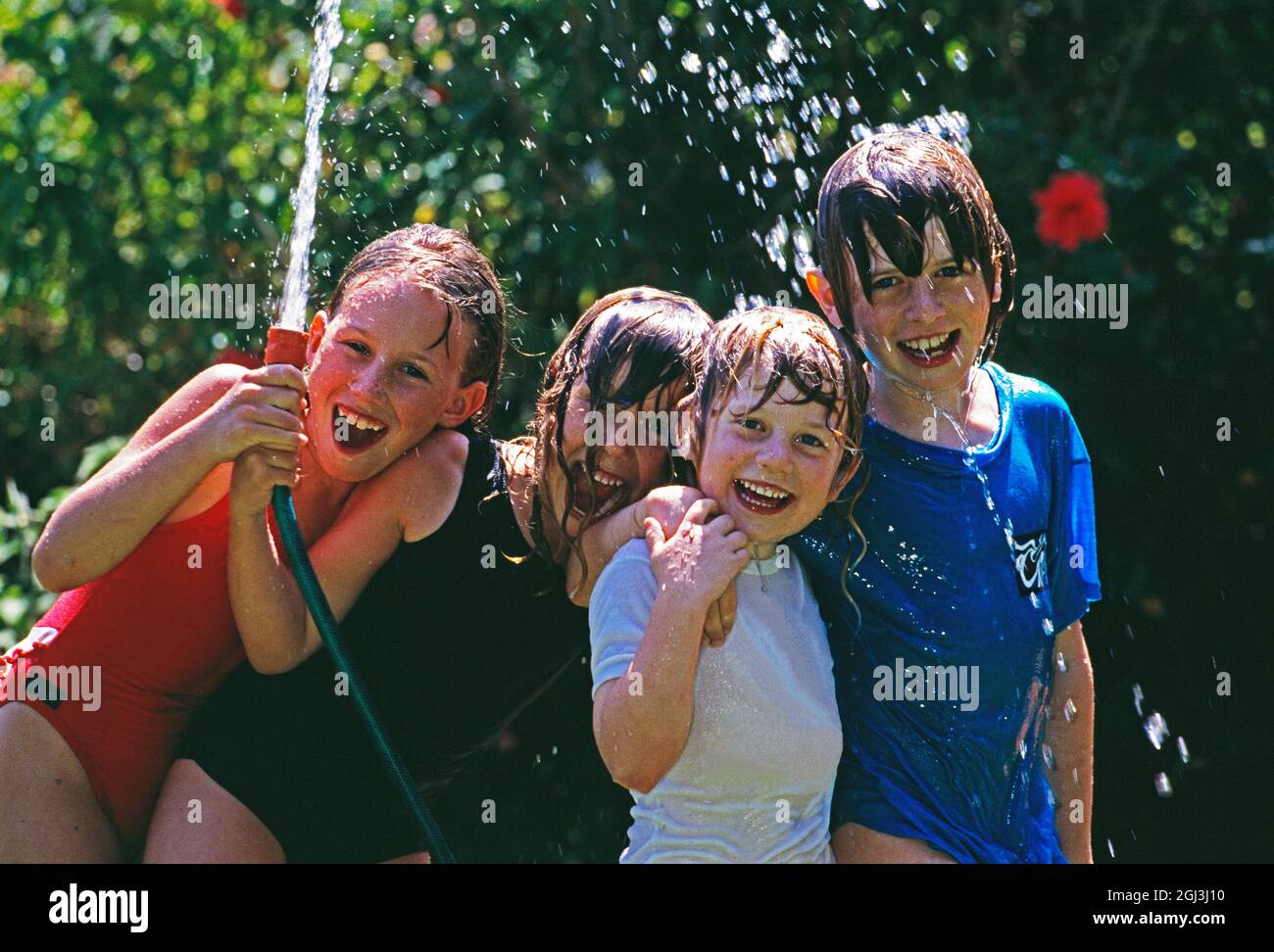 Group of children playing outdoors with water hose. Stock Photo