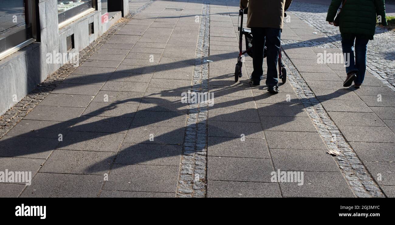 long shadows of two elderly people on the pavement of the sidewalk, man walking with a walking aid Stock Photo