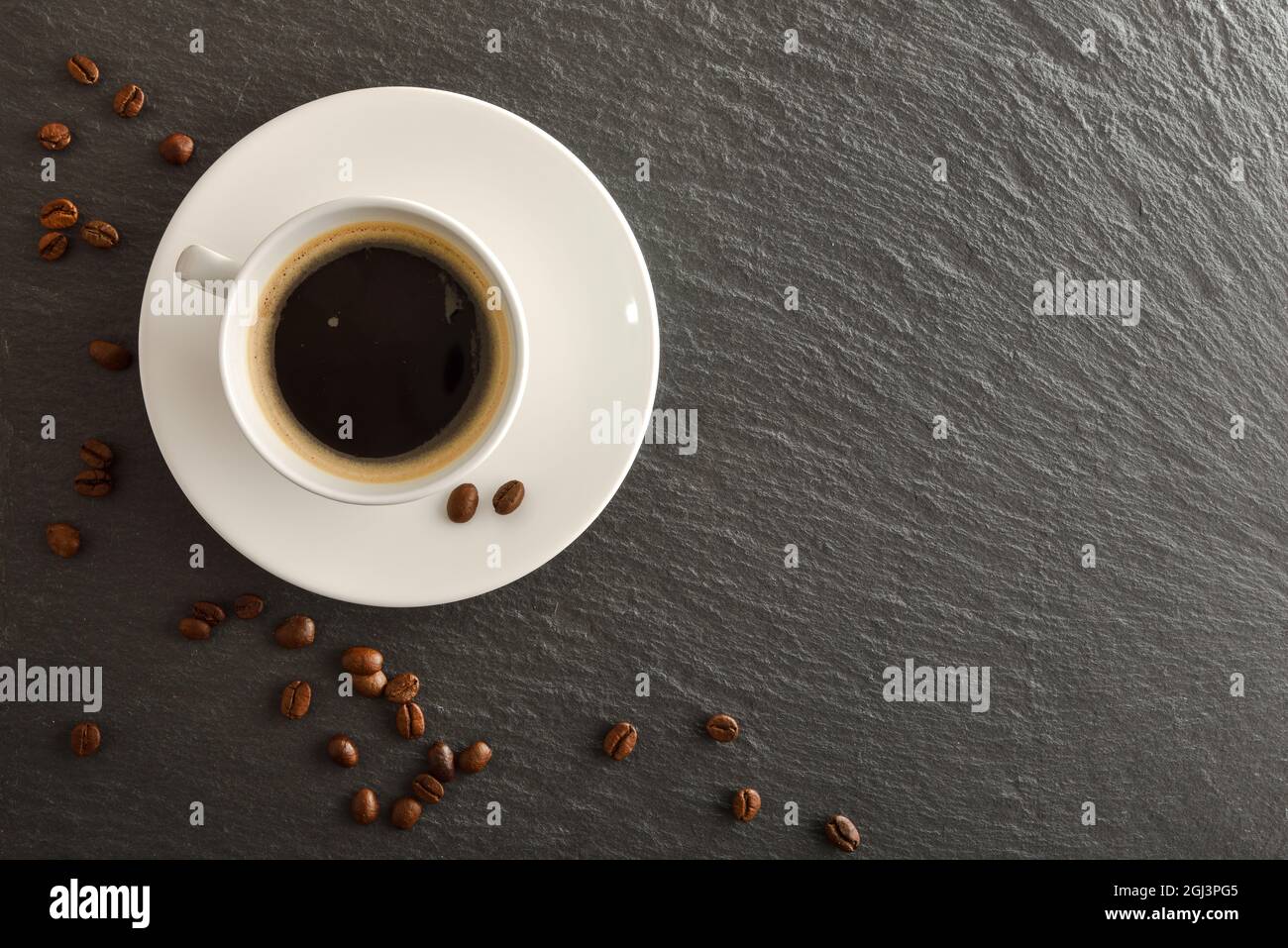 White cup of coffee on plate and beans on slate table with blank space. Top view. Horizontal composition. Stock Photo