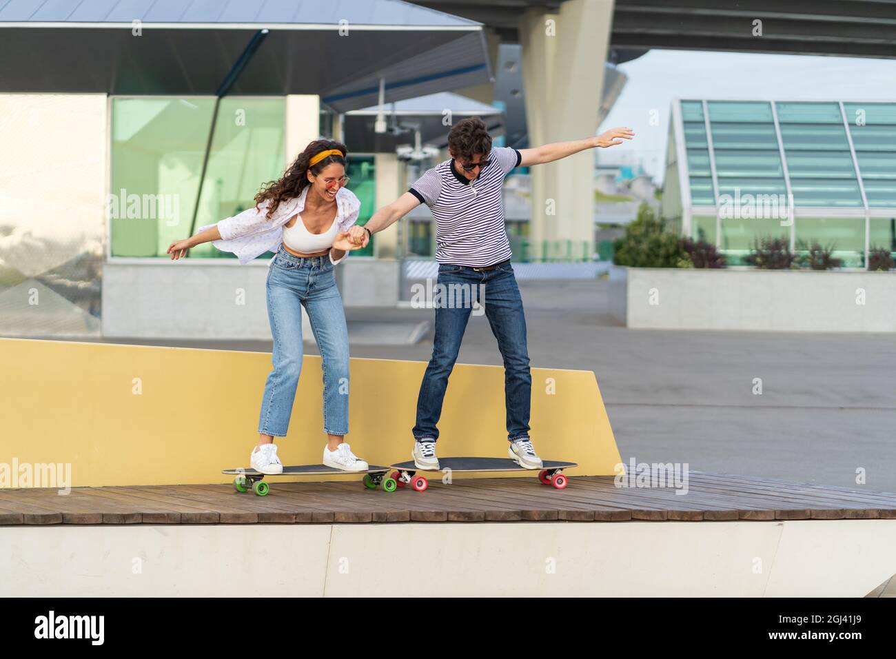 Active young skaters couple learn to ride longboard together hold hands laughing stand on skateboard Stock Photo