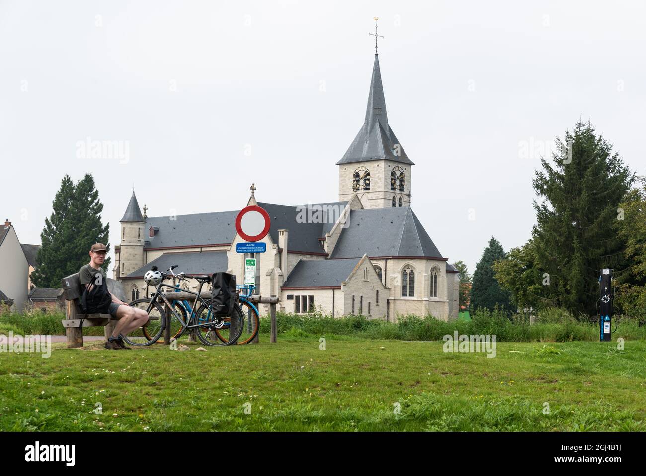 Vilvoorde,  Flemish Brabant - Belgium - 09 01 2021: Man resting with his bicyle with a white church and  green surroundings in the background Stock Photo