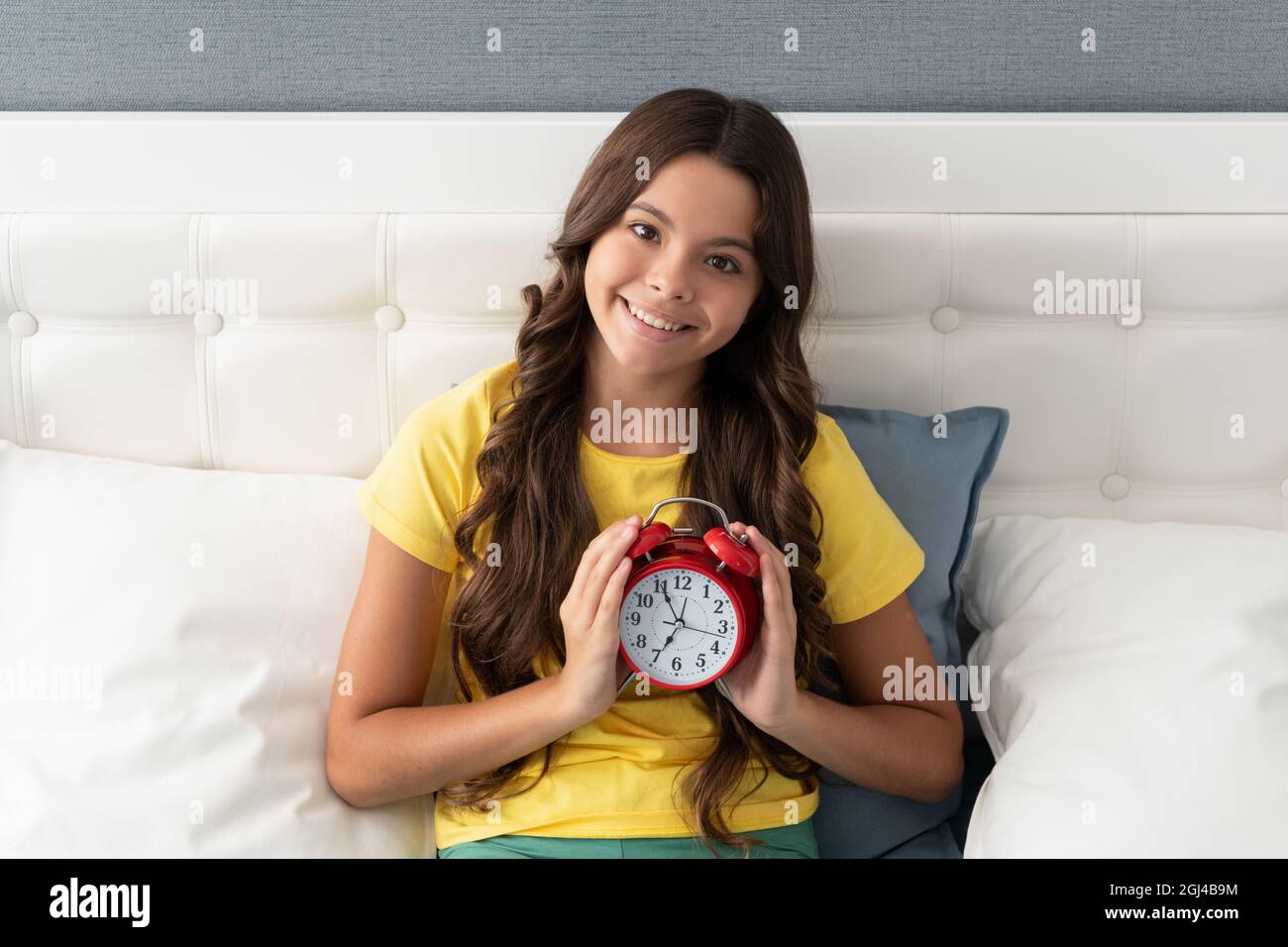 Good morning. Happy kid hold alarm clock in bed. Morning time. Wakening