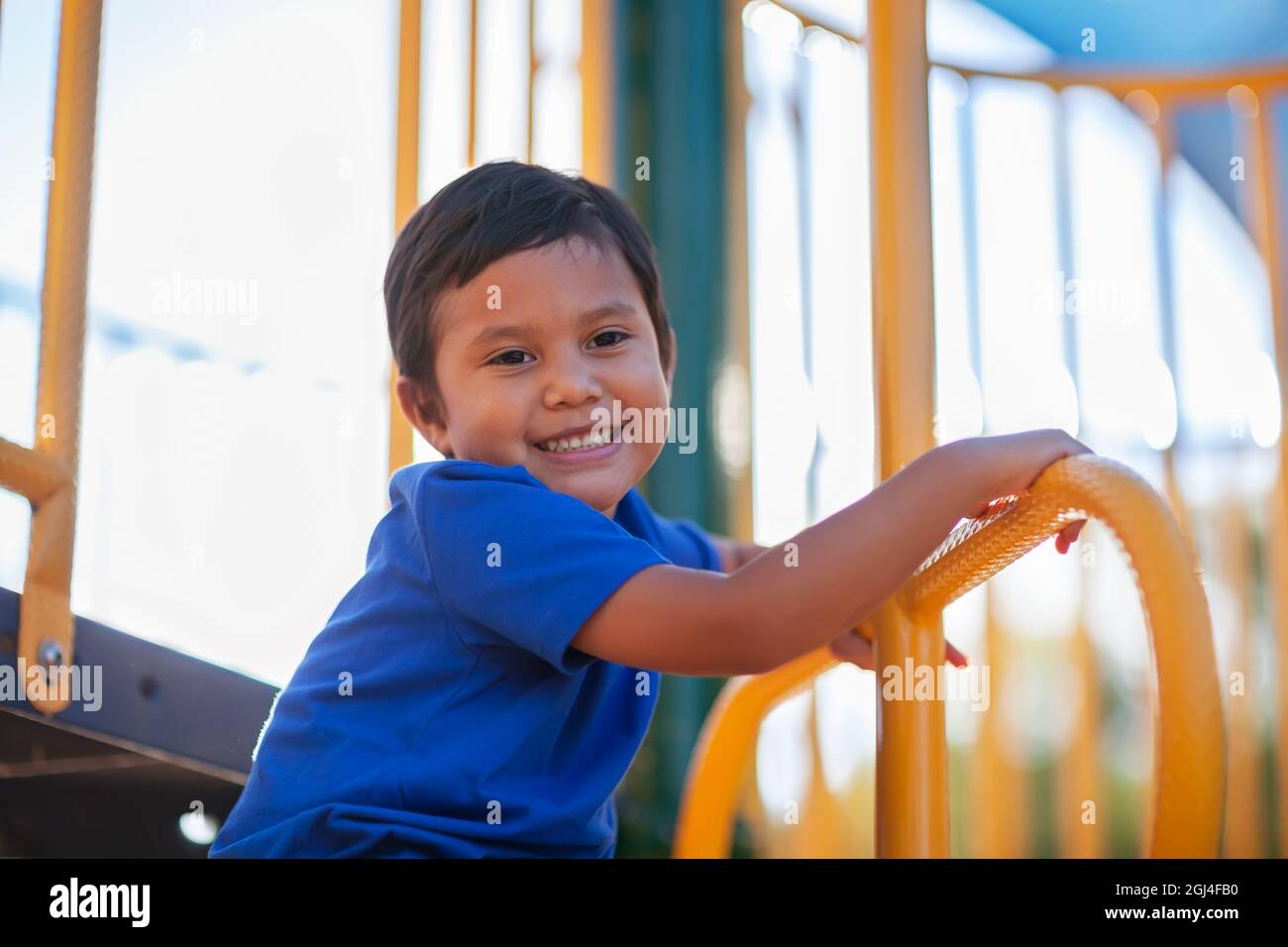Young boy looking down and smiling while having fun climbing a jungle gym monkey bar. Stock Photo