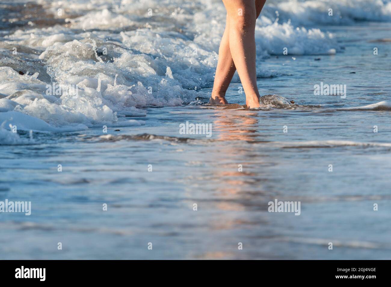Beautiful legs of a young woman walking on a beach with waves rolling