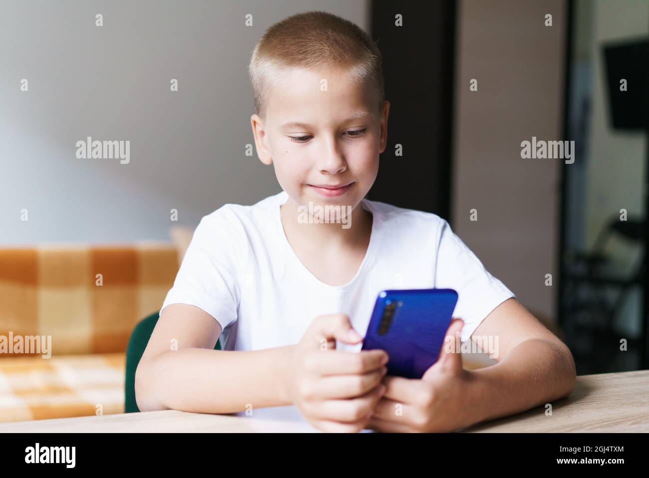 Happy cute baby, kid, son sitting at table relaxing, having fun with mobile  phone, playing games, watching funny videos on social networks, laughing,  enjoying using mobile phone at home Stock Photo -