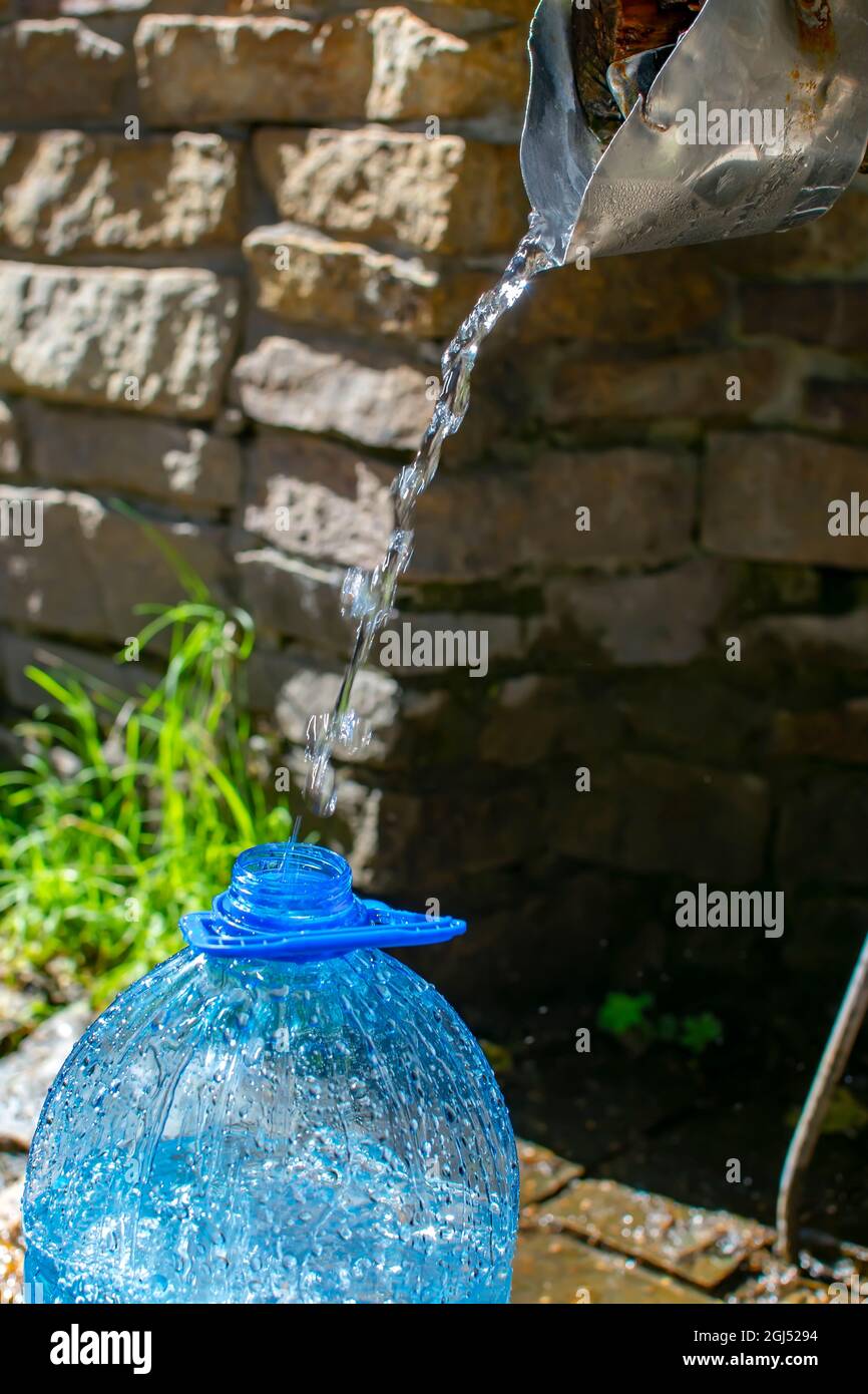 the neck of a plastic five liter bottle, into which a stream of pure natural, useful, life giving water is poured from an equipped, man made spring Stock Photo