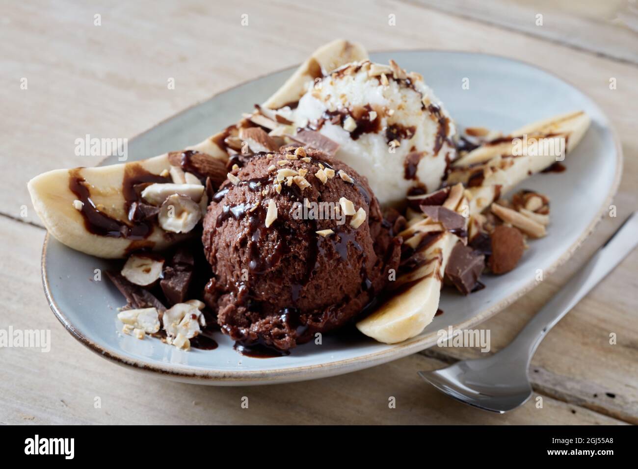 From above of delicious balls of chocolate and vanilla ice cream served on plate with banana slices decorated with nuts and syrup Stock Photo