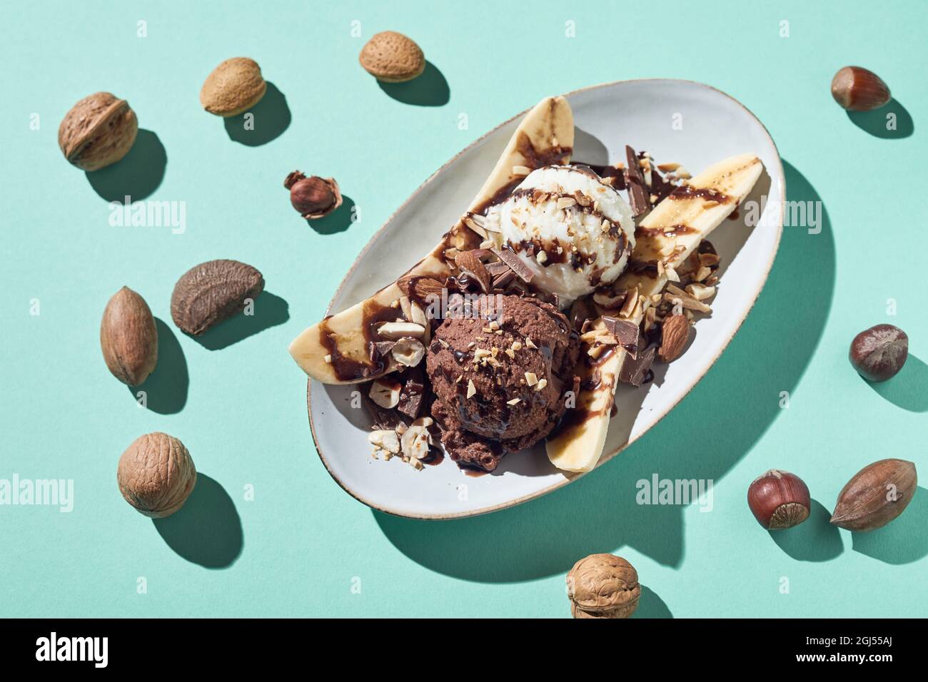 Top view of appetizing banana split dessert with vanilla and chocolate balls of ice cream garnished with syrup and hazelnuts served on light blue back Stock Photo