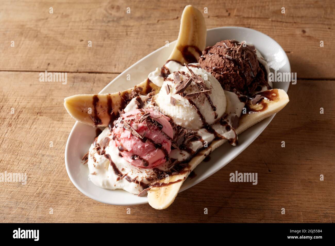 From above of plate with appetizing banana split dessert with balls of ice cream and chocolate syrup served on wooden table Stock Photo