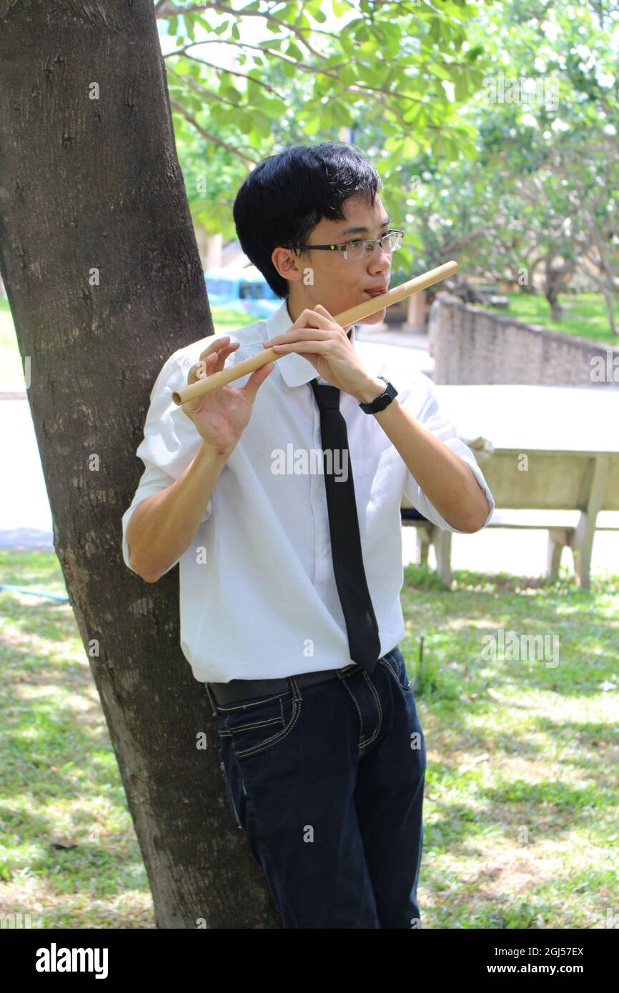 Young man playing the flute next to a tree in the garden Stock Photo