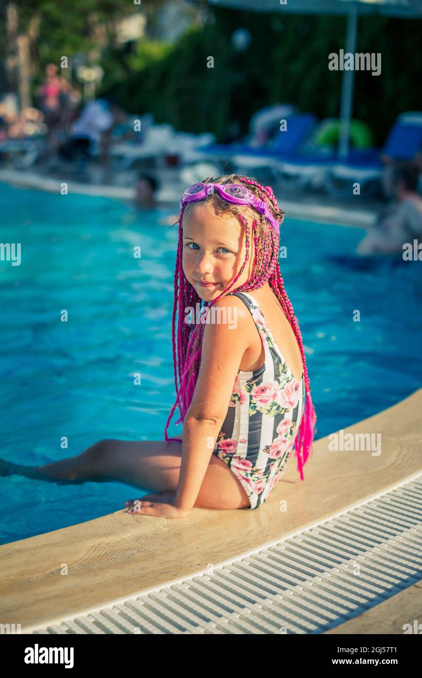 A girl with pink pigtails seats by the pool smiling Stock Photo