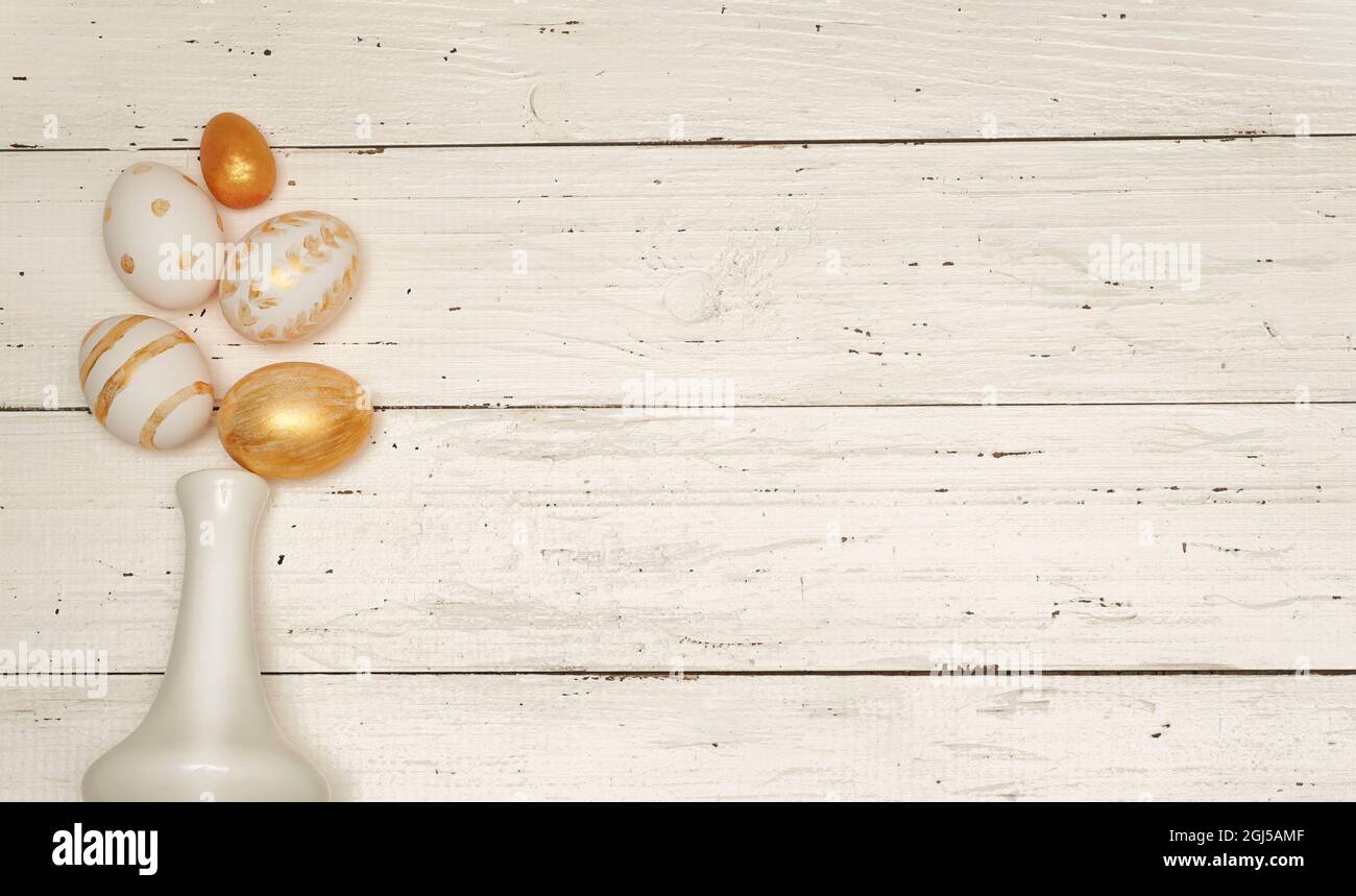 Golden Easter eggs and white vase on rustic old wooden background. Trendy Easter flat lay composition. Copy space for text. Minimal Easter concept. Ea Stock Photo