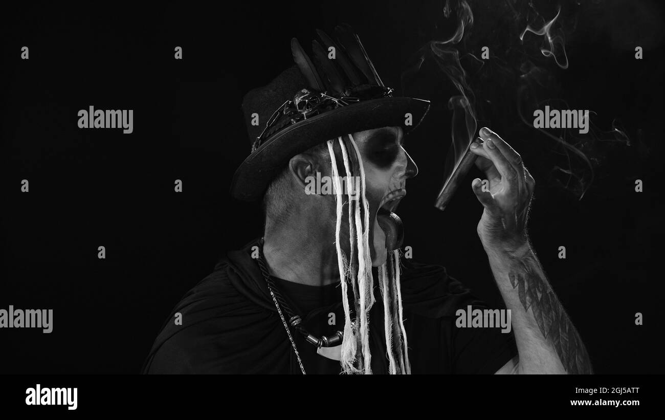 Scary guy in carnival costume of Halloween skeleton smoking cigar, making faces, showing tongue Stock Photo