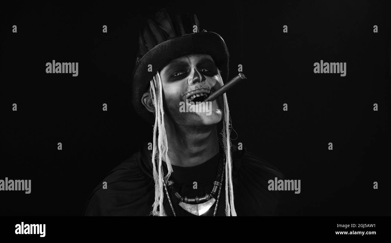 Frightening man in skeleton Halloween cosplay costume smoking cigar, making faces, smiling Stock Photo