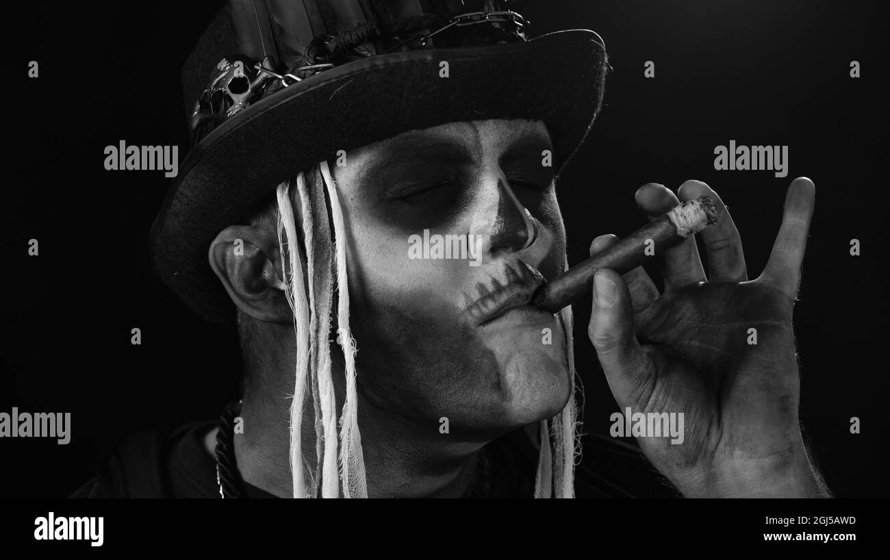 Frightening man in skeleton Halloween cosplay costume smoking cigar, making faces Stock Photo