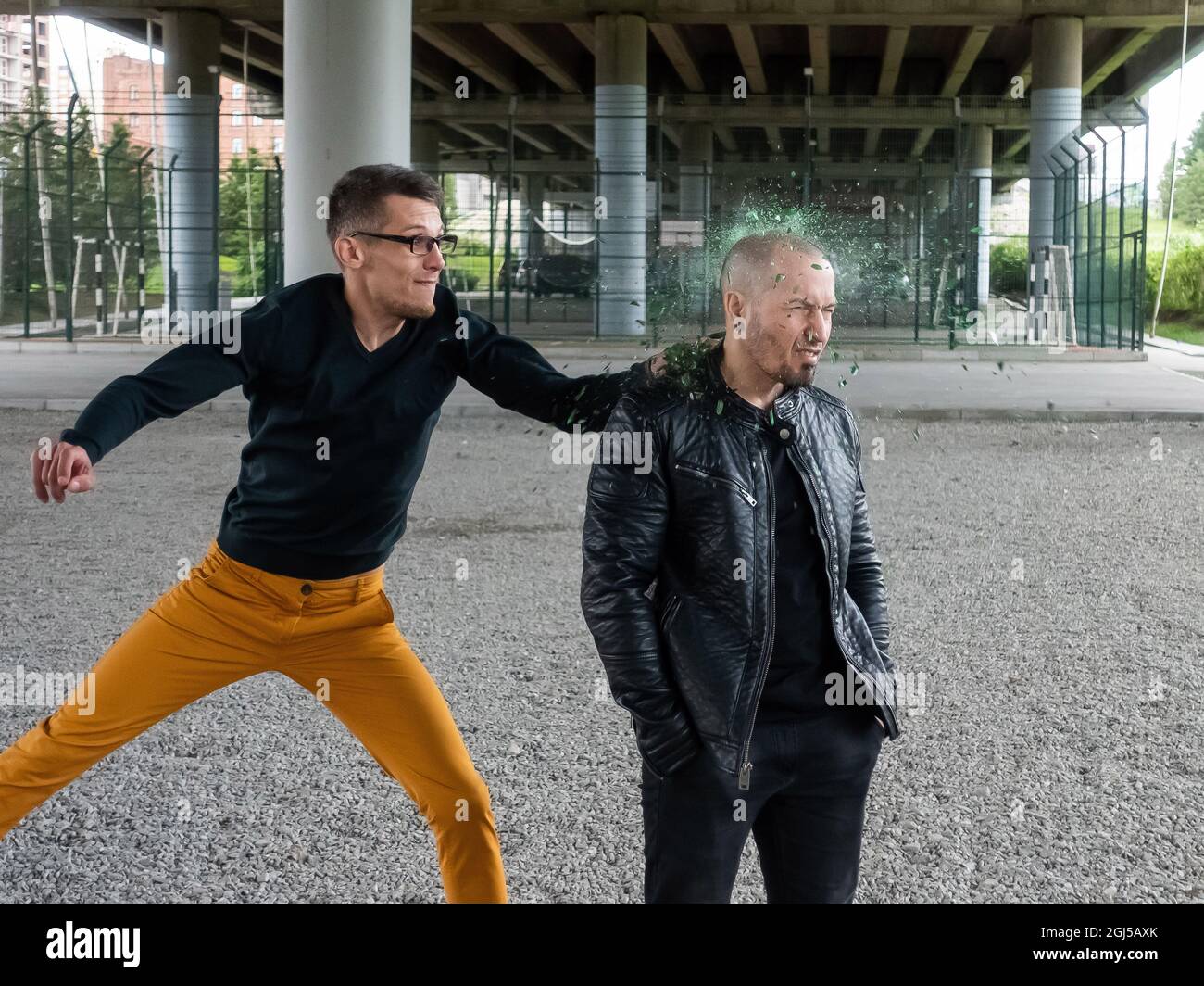 Nerd attacks a shaven-headed bandit and smashes a bottle on his head. A fight between men Stock Photo