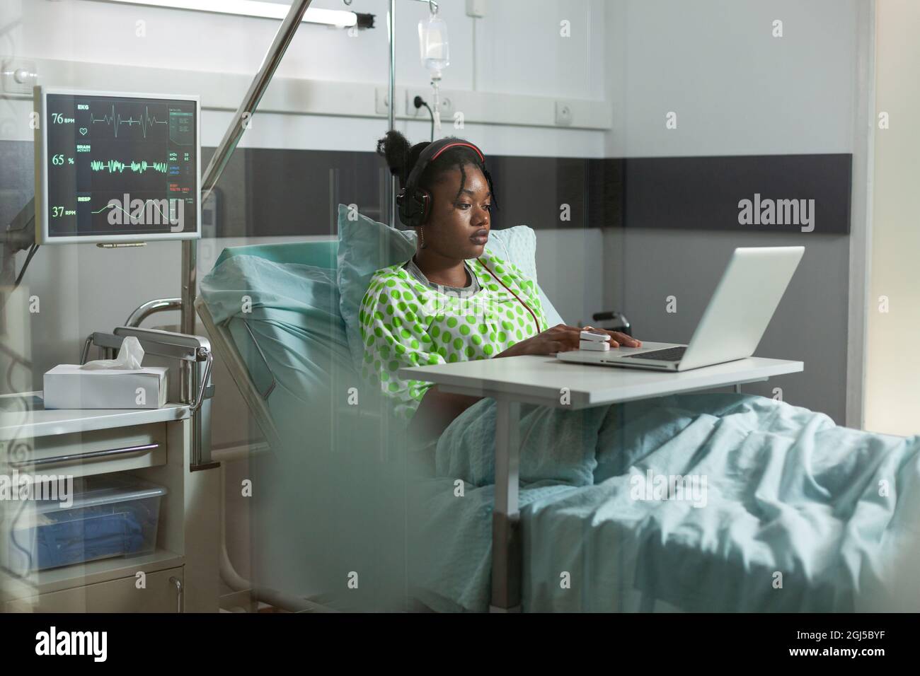 Sick young patient with headphones using laptop in hospital ward ...