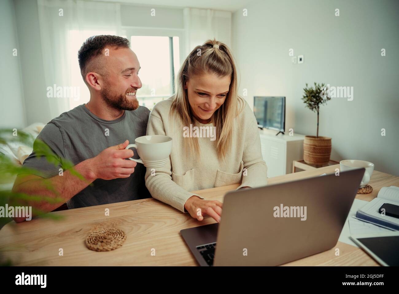 Cute caucasian couple sitting at kitchen table typing on laptop Stock Photo