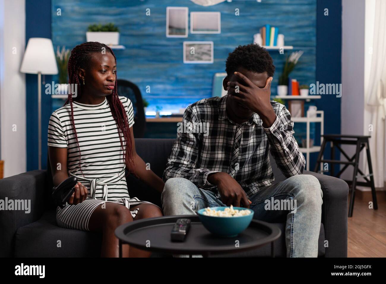 Disappointed black couple losing at video game on TV with controllers. African american lovers playing with console and joysticks on television at home. Afro people with enjoyment Stock Photo