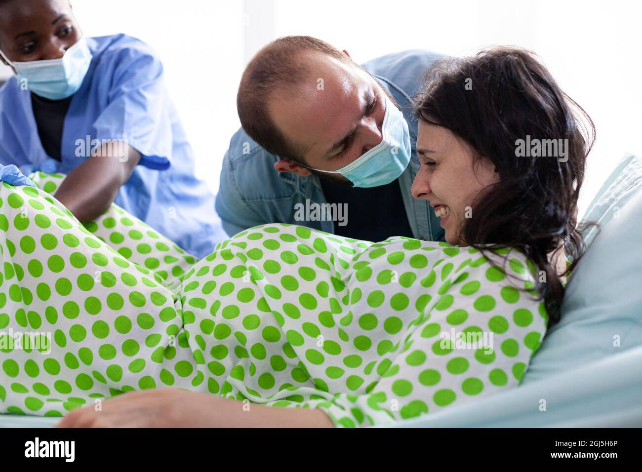 Young woman in pain pushing for childbirth at maternity while african american nurse assisting in hospital ward. Person giving birth while laying in bed and father of baby holding hand Stock Photo