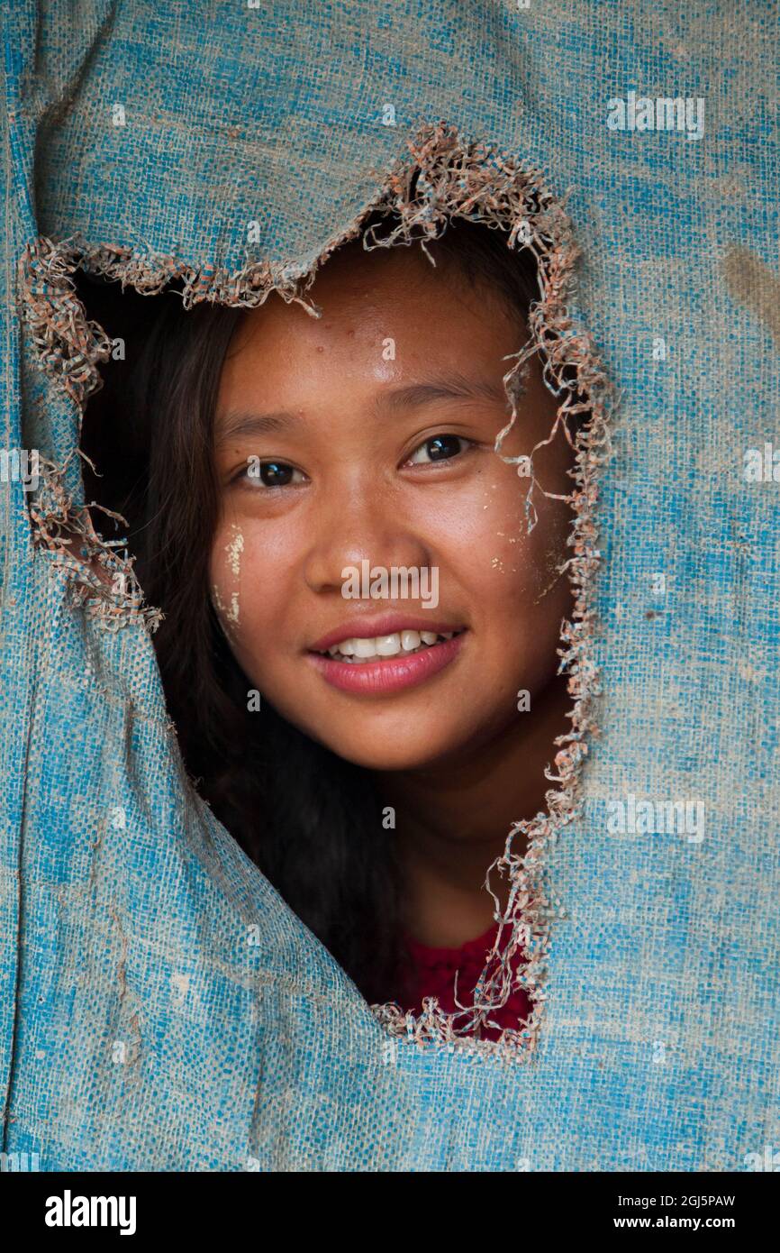 Portrait of a young Burmese girl smiling through a piece of hanging fabric in Myanmar. Stock Photo