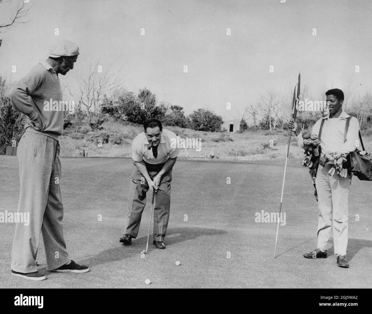 Douglas Bader lines up his putt on the green at the Mid Ocean Club Course in Tucker's Town Bermuda watched by his friend Archie Compston the clubs professional 1957 Stock Photo