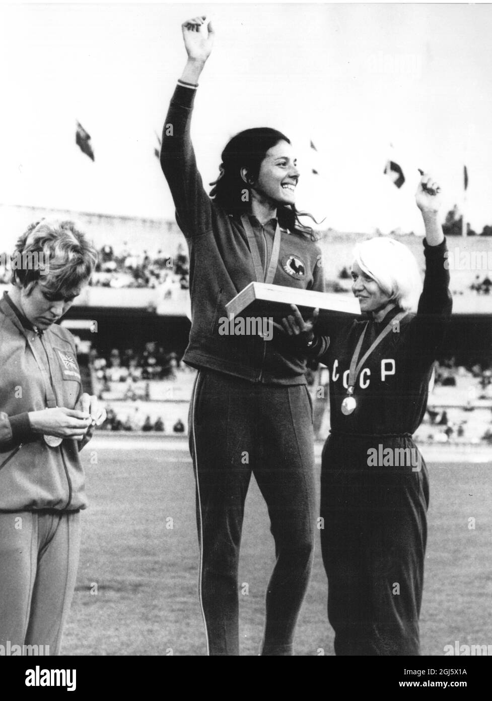 As Britain 's Lilian Board ( left ) stands unsmilingly by , France 's Colette Besson ( centre ) waves to the crowds after receiving her gold medal for winning the final of the Women ' s 400 metres at the 19th Olympic Games . Her time of 52.0 seconds equalled the Olympic record . Miss Board was second and Russia ' s Natalia Pechenkina ( Right ) gained the bronze medal . 17 October 1968 Stock Photo