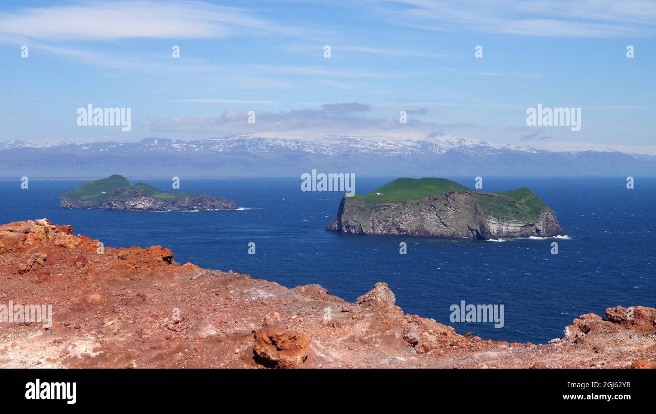 Beautiful view across the sea from Eldfell volcano, Heimaey (Iceland), of Eyjafjalljökull volcano on the horizon. Two grassy islands in between. Stock Photo