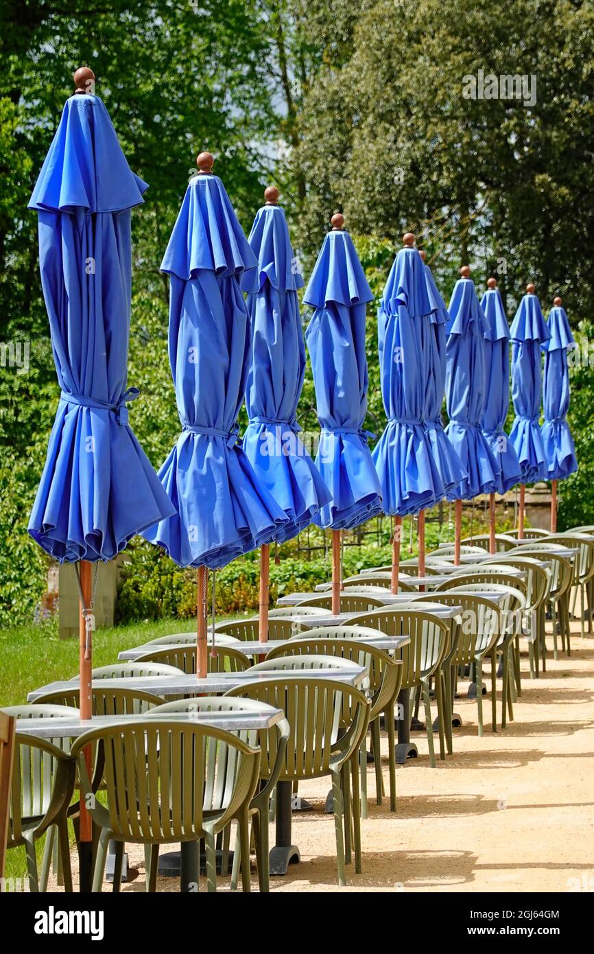 Row of outdoor tables chairs & folded blue parasols outside hotel bar with summer season weather too cold & windy for guests to use in May England UK Stock Photo