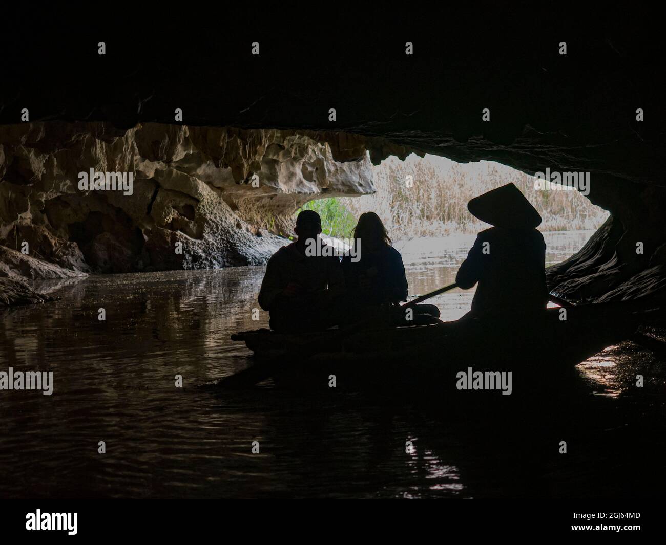 Vietnam, Van Long Nature Reserve. Woman rowing boat with tourists exploring cave. Stock Photo