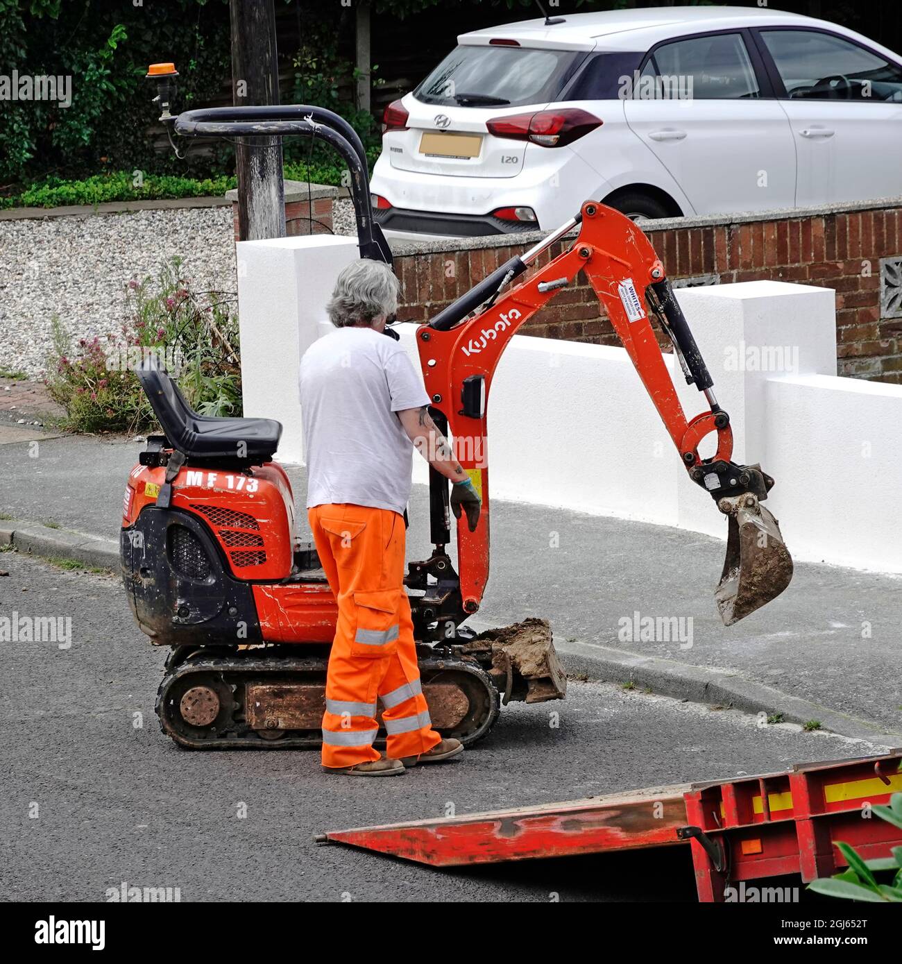 Mini digger excavator on hire lorry truck driver steering digger machine on or off vehicle ramp on road delivery or collection from building site UK Stock Photo